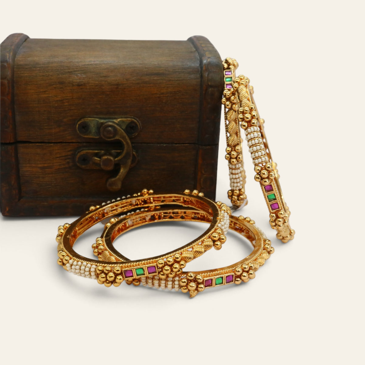 Close-up of four slim gold-tone bangles with rows of pearls and square red and green semi-precious stones