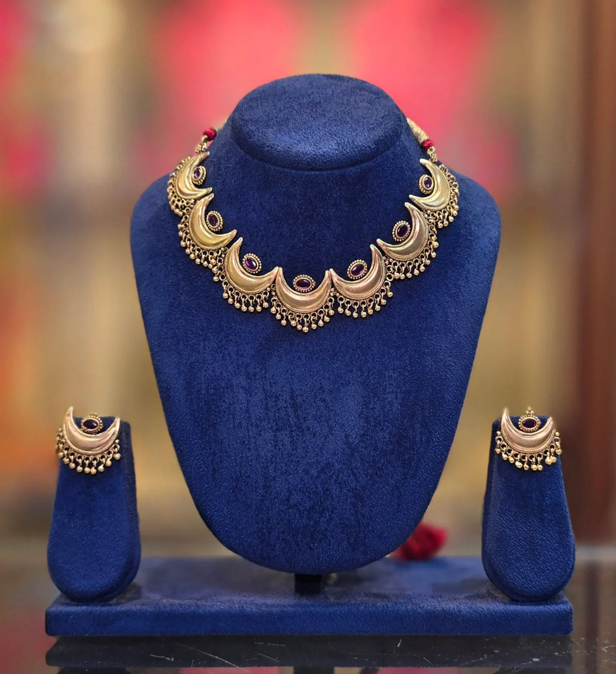 Gold plated Chandrakor necklace on a display bust – crescent links with red stones and gold bead drops, shown with matching earrings