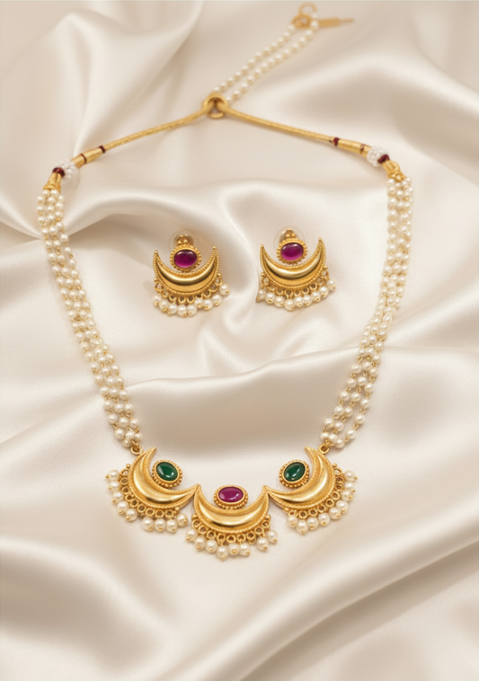 Gold plated Chandrakor pearl necklace with ruby and green stones and stud earrings on ivory satin