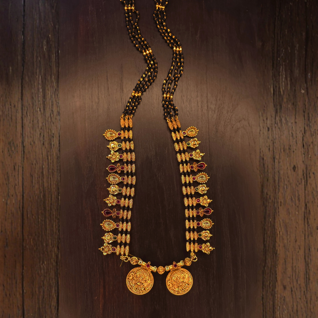 Long antique gold plated mangalsutra with black beads and double coin pendant on dark wood