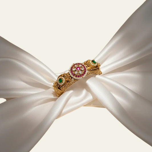 Jija Jewellery Heritage Glow Kundan Kada featuring gold-plated metal, ruby and emerald stones on white silk fabric.