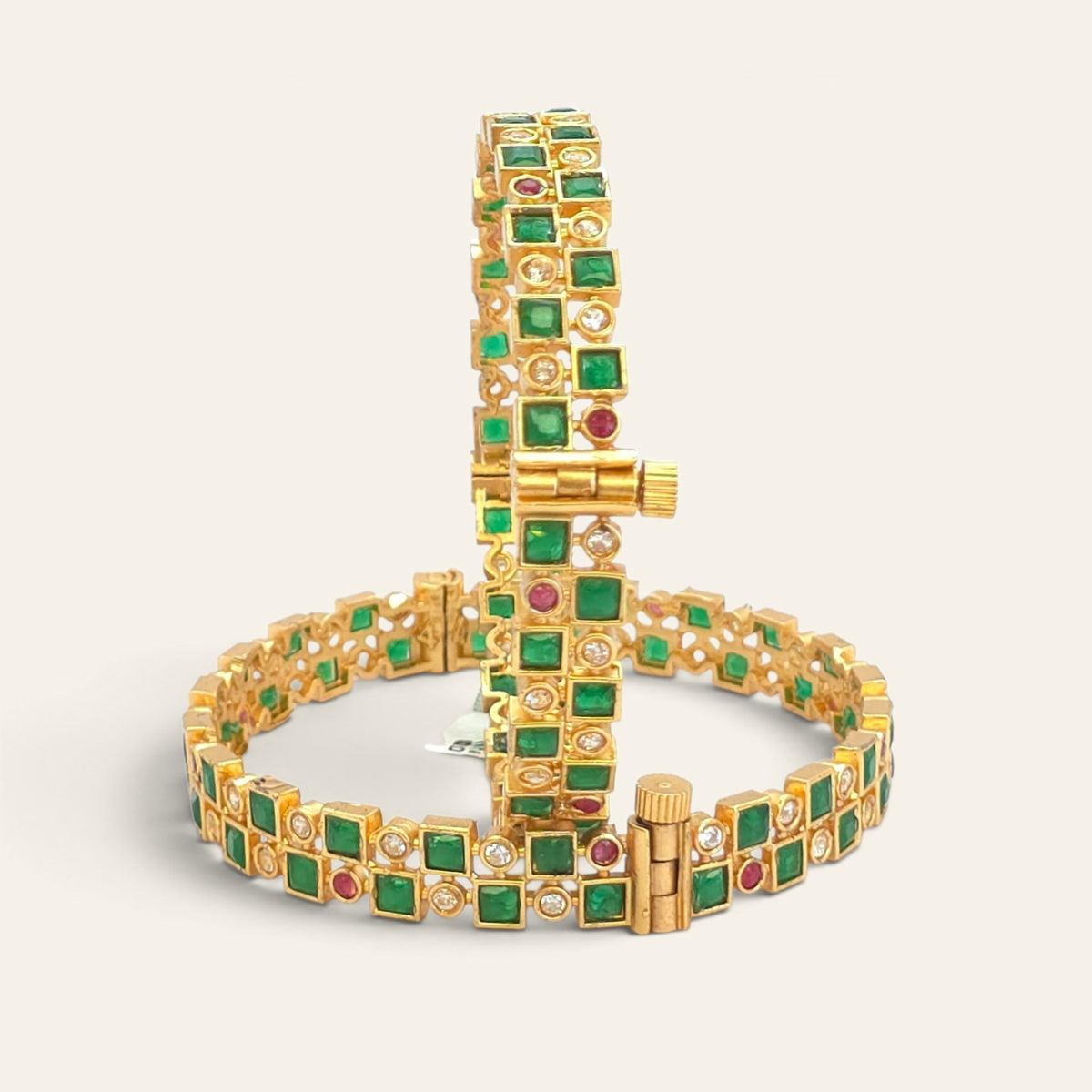 Emerald green gold plated bangle displayed upright on stand with second bangle in background