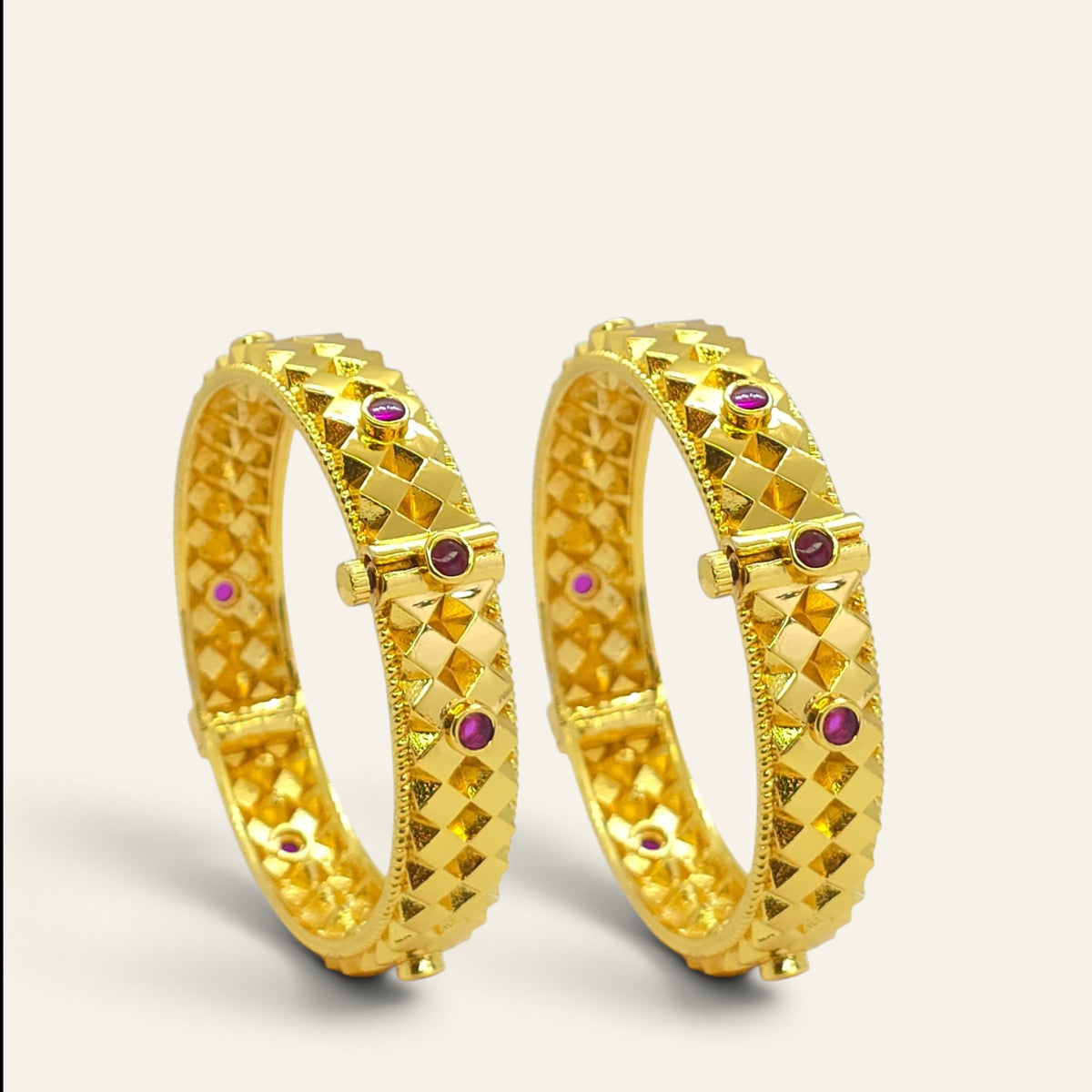 Diamond cut gold plated bangles with ruby accents, pair standing upright, angled view
