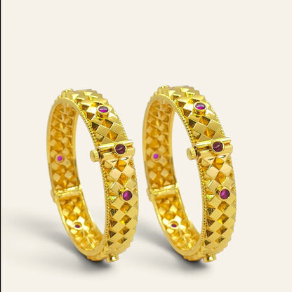 Diamond cut gold plated bangles with ruby accents, pair standing upright, angled view