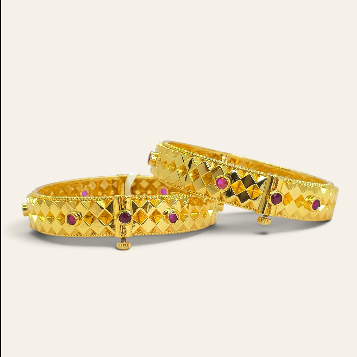 Diamond cut gold plated bangles with ruby stone accents, pair lying flat showing openable hinge