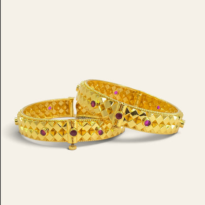 Close-up of diamond cut gold plated bangles with ruby accents, overlapping pair