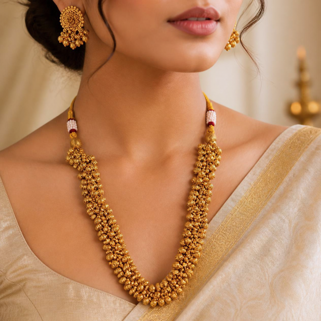 Woman wearing a long gold plated ghungru necklace and ghungru earrings with a cream silk saree