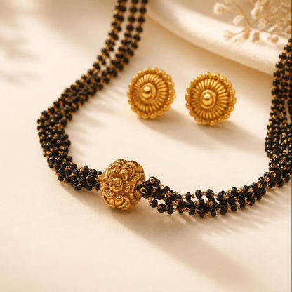 Gold plated black bead mangalsutra with multi-strand design and floral centerpiece bead, paired with circular stud earrings
