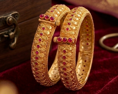 Gold bangles with red stones on a red velvet surface next to a wooden box.