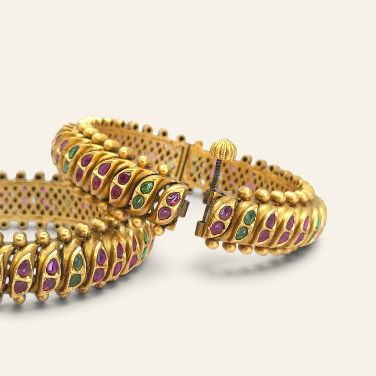 Close-up of antique gold look kada bangles with red and green semi-precious stones and screw openable clasp