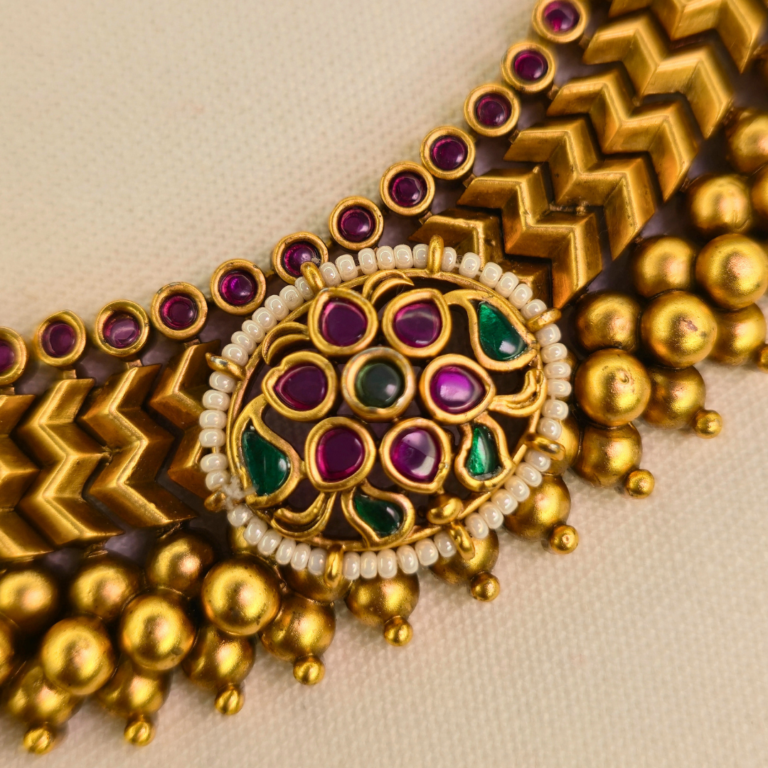 Vazartik Thushi necklace close-up showing gold beads and ruby stone medallion