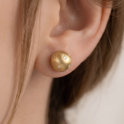 Pair of matte gold dome stud earrings with scattered star-set cubic zirconia, on white background