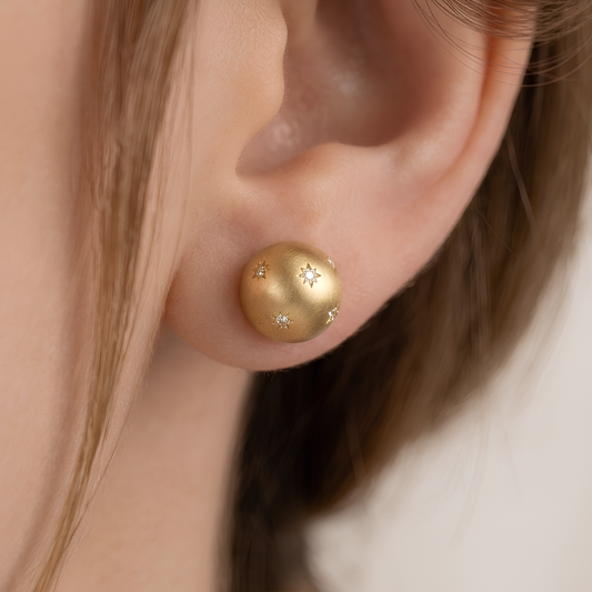 Pair of matte gold dome stud earrings with scattered star-set cubic zirconia, on white background