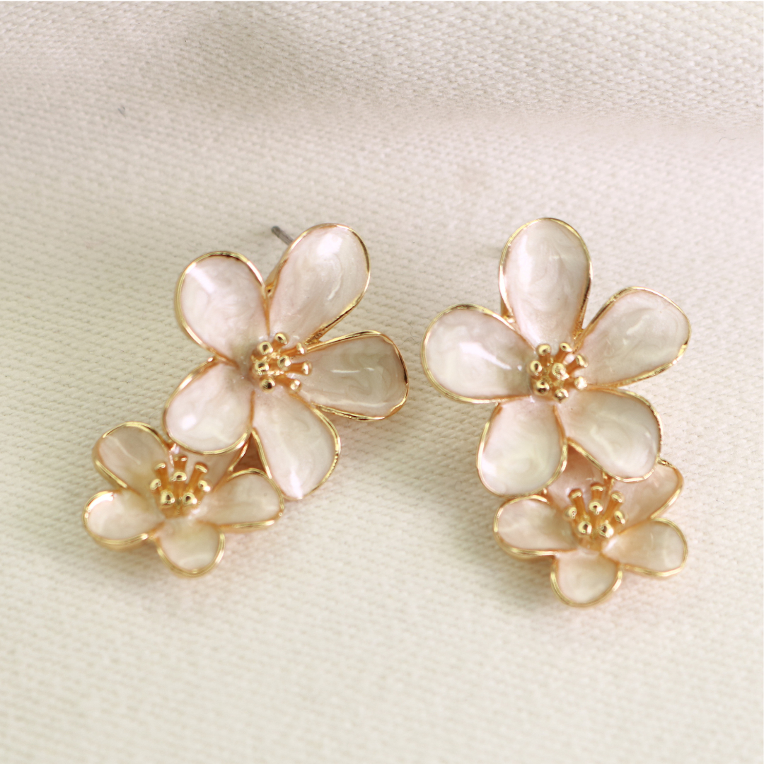 Cream and ivory enamel floral stud earrings with gold-tone outline on fabric