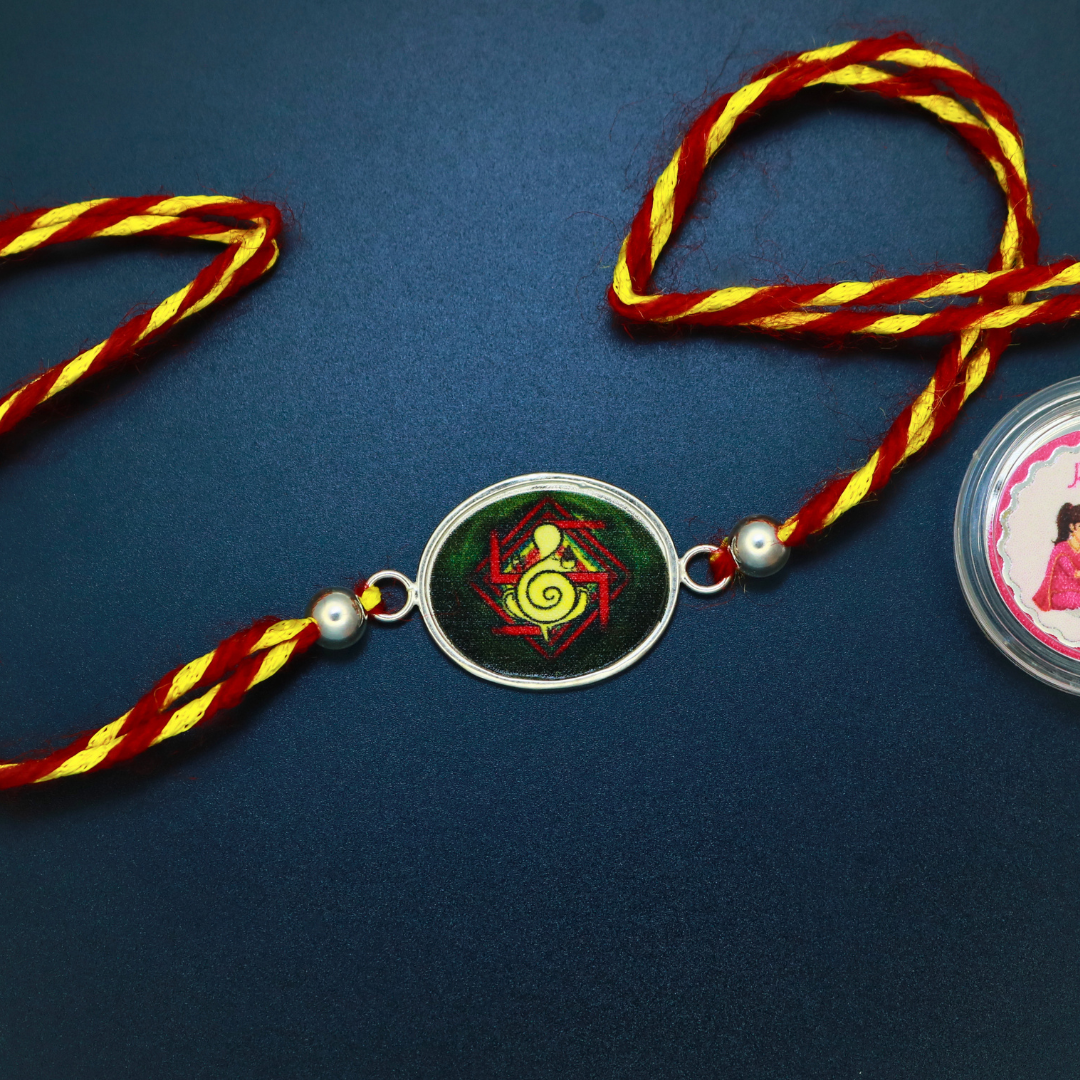 Oval sterling silver Ganesha yantra rakhi in meenakari enamel with silver beads on twisted red and yellow cord