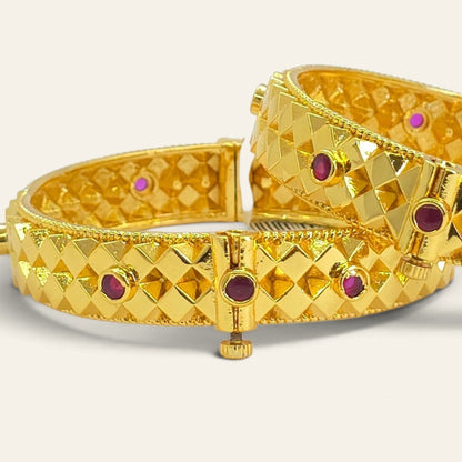 Close-up of Ashtapailu glossy polish gold plated bangles with ruby accents, overlapping pair