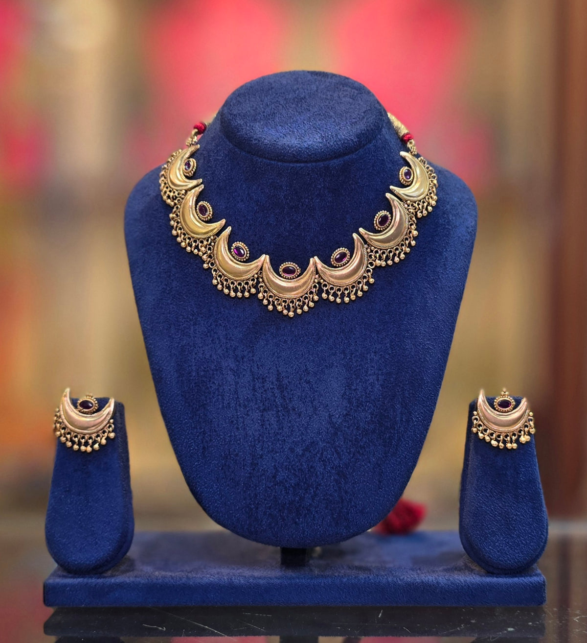 Gold plated Chandrakor necklace on a display bust – crescent links with red stones and gold bead drops, shown with matching earrings
