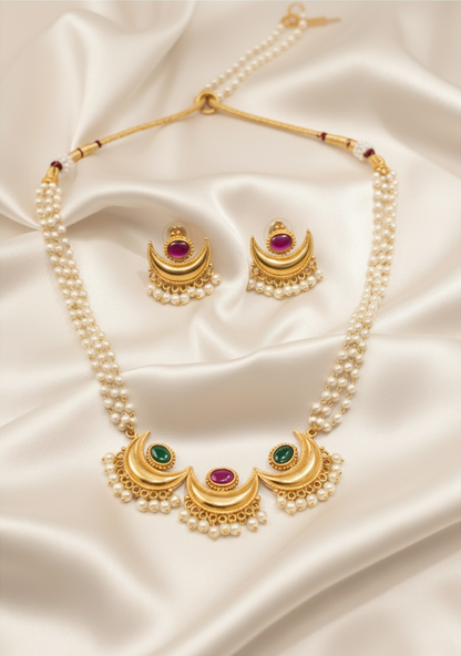 Gold plated Chandrakor pearl necklace with ruby and green stones and stud earrings on ivory satin