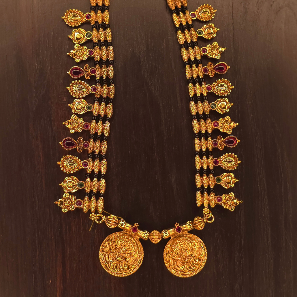 Close-up of double Lakshmi coin pendant and antique gold charms on black bead mangalsutra