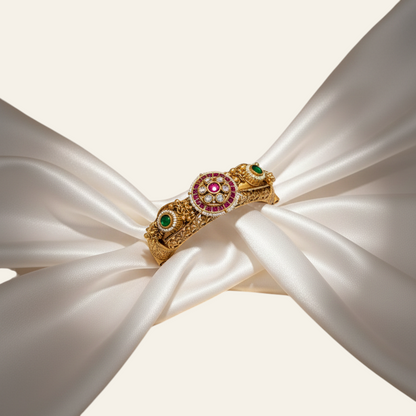 Jija Jewellery Heritage Glow Kundan Kada featuring gold-plated metal, ruby and emerald stones on white silk fabric.