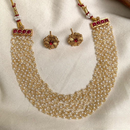 Multi-layer pearl necklace with ruby-set end caps and matching stud earrings on ivory cloth