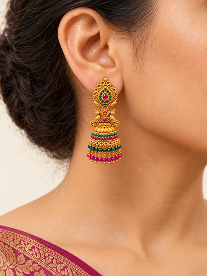 Model wearing gold-plated peacock jhumka earring with pink and green bead tassels
