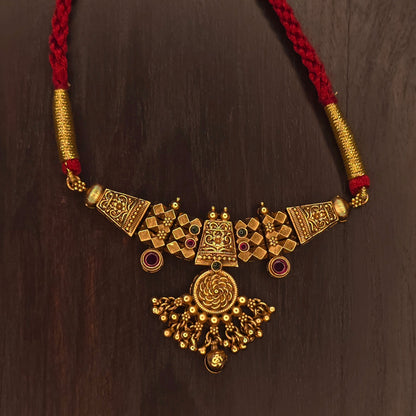Close-up of gold Thushi necklace pendant with spiral rosette centre and checkered base on red braided dori – Maharashtrian jewellery
