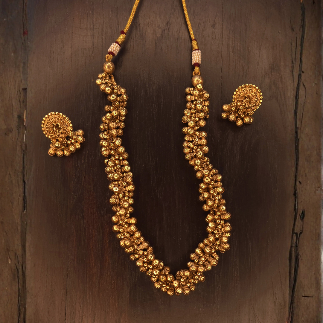 Long ghungroo necklace on gold dori with pearl-bead accents and matching earrings on dark wood